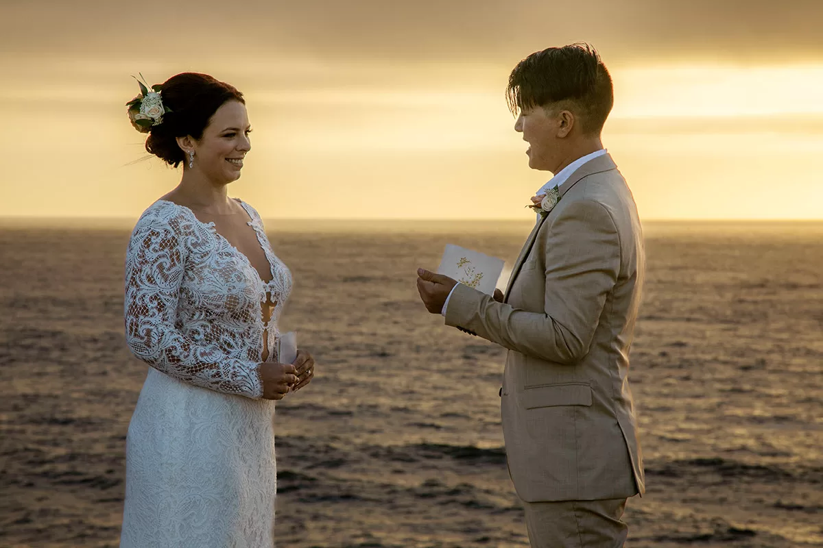 Bride and groom reading their wedding vows to each other with sunset behind wedding photo